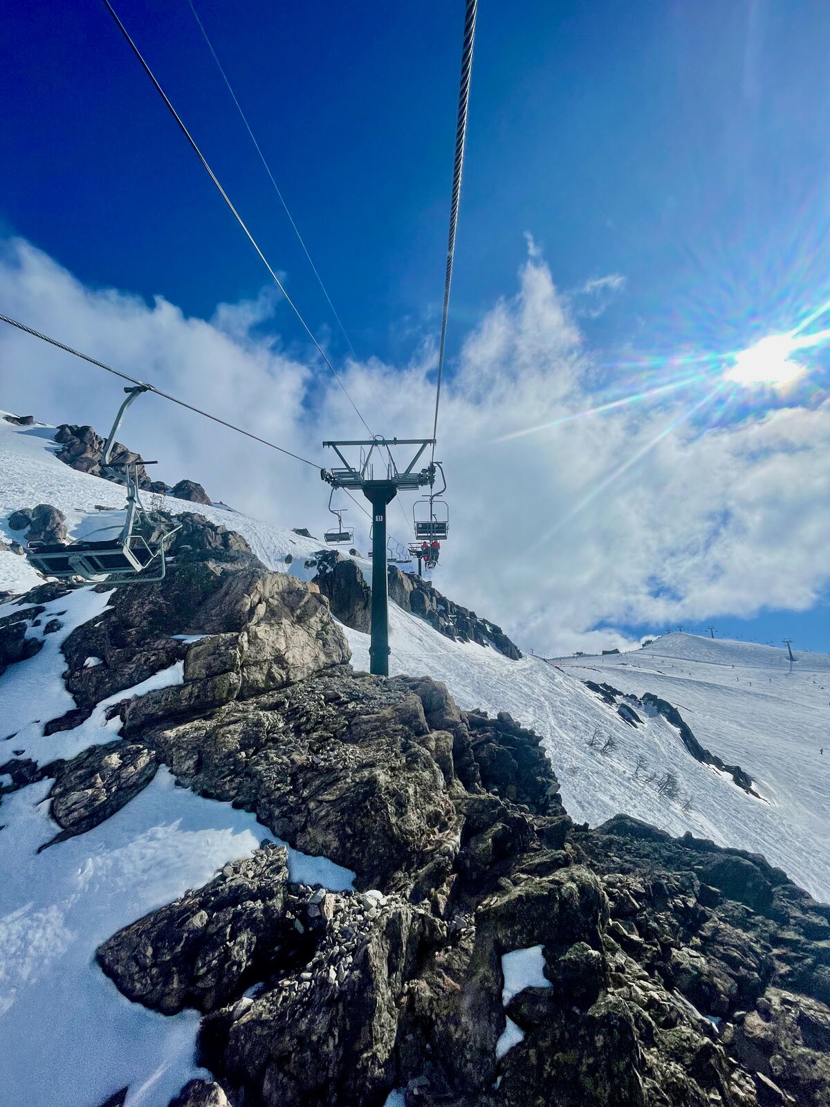 Chairlift running over rocky snowy terrain at Cerro Catedral under blue sky